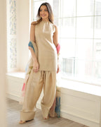 A woman wearing a beige three-piece raw silk suit with a floral printed organza dupatta, consisting of a sleeveless top, wide-leg trousers, and a headscarf.